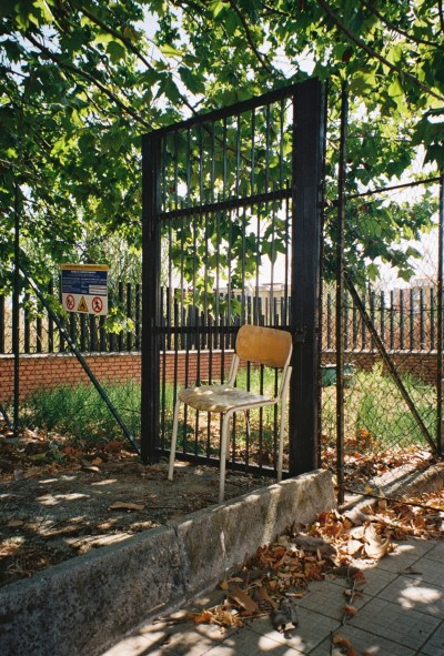 A photo of a chair in front of a fence gate, outdoors